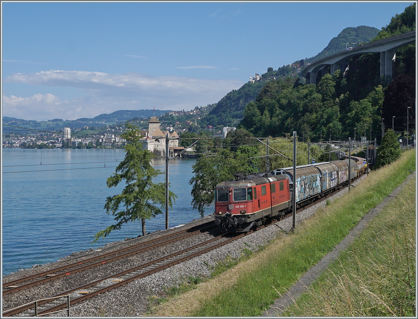 Die SBB Re 4/4 II 11286 (Re 420 287-7) ist vor dem Hintergrund des Schlosses von Chillon bei Villeneuve mit einem Güterzug unterwegs. 

5. Juni 2024
